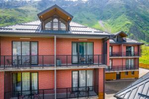 a red brick building with a balcony and mountains in the background at Kazbegi MaNa Apartment N 111 in Kazbegi