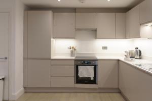 una cucina con armadi bianchi e forno di Gorgeous New 2 Bed Flat - 2 August House a Londra