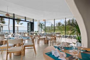 un restaurante con mesas, sillas y ventanas grandes en Dhawa Ho Tram, en Ho Tram