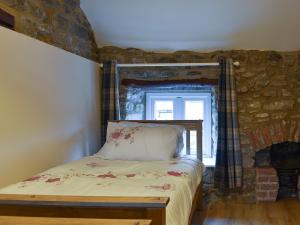 1 dormitorio con 1 cama con pared de piedra en Corner Cottage, en Longstone