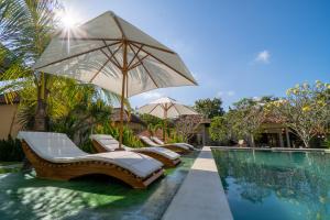 een zwembad met ligstoelen en een parasol naast een zwembad bij IKIGAI Uluwatu Beach in Uluwatu