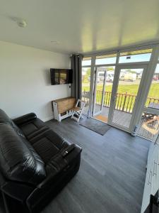 a living room with a black leather couch and a balcony at Cozzzy Seaside Retreat in Mablethorpe