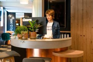 una mujer de pie detrás de una mesa con plantas en Ibis Styles Colmar Centre en Colmar