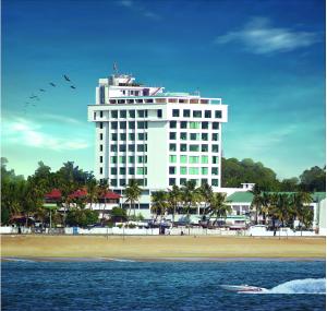ein großes weißes Gebäude am Strand mit einem Boot in der Unterkunft The Quilon Beach Hotel and Convention Center in Kollam