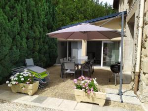 un patio con una mesa con sombrilla y flores en Le gite du mazagran, 