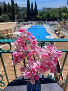 een vaas met roze bloemen op een tafel naast een zwembad bij Maria Studios in Paleokastritsa