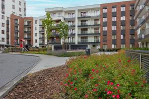 Stunning Family Apartment Ursynów with Parking & Balcony by Noclegi Renters في وارسو: حديقة فيها ورد احمر امام مبنى