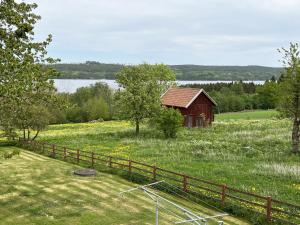 um celeiro vermelho num campo com uma cerca em Cozy red cottage in the countryside outside Vimmerby em Gullringen
