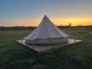 una tienda blanca sentada en una plataforma de madera en un campo en FARM LIVING, en Gottby