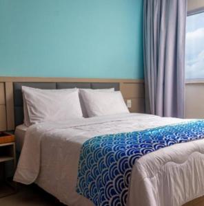 a bed with a blue and white blanket and a window at Suite - Aqualand Suites in Salinópolis