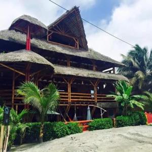 a building with a straw roof and some palm trees at Hotel Bambu Mompiche in Mompiche