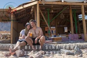 Ein Mann und eine Frau sitzen auf einem Schild am Strand in der Unterkunft New Bella Sina Camp in Nuweiba
