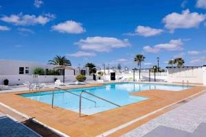 a large swimming pool with a wooden deck and a blue sky at Apartamento Los Marinos in Tías