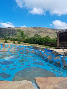 a swimming pool with blue water and mountains in the background at Chalés Encantos da Serra in Carrancas