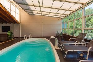 a swimming pool in a room with chairs and a tub at Hotel Morada Del Este in Canoas
