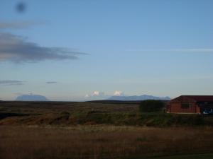 un campo con una casa roja y montañas a lo lejos en Grímstunga Guesthouse road 864 Grimsstaðir Hólsfjöllum en Víðirhóll