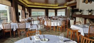 um restaurante com mesas e cadeiras brancas e janelas em Up Pateira Hotel em Fermentelos