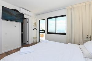 a white bedroom with two beds and a flat screen tv at נוף העמק - דירה מהממת עם נוף עוצר נשימה in Nof Kinneret
