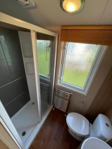 a bathroom with a shower and a toilet and a window at Millfields Holiday Park - Diamond Deluxe - Coastal Caravan Breaks in Ingoldmells