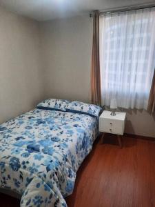 a bedroom with a bed with a blue floral bedspread and a window at Hermoso dpto en condominio residencial en estreno in Paucarpata