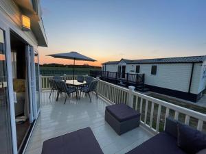 a deck with a table and chairs and an umbrella at Millfields Holiday Park - Knightsbridge Deluxe - Coastal Caravan Breaks in Ingoldmells