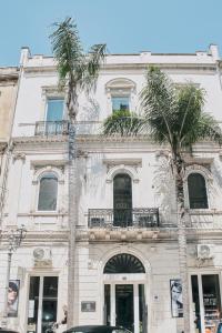 a white building with two palm trees in front of it at Appartamenti Luxury Greco in Brindisi