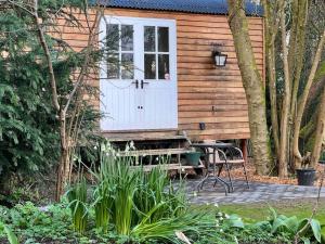 a wooden cabin with a white door and a bench at Tranquil Spot Shepherds Hut in Cinderford