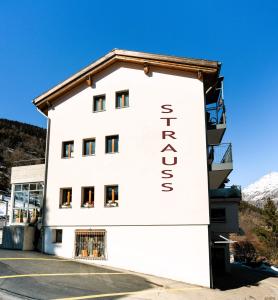 a white building with the sign for the hotel at Kulinarik & Geniesser Hôtel STRAUSS in Fiesch