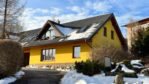 a yellow house with a black roof in the snow at SnežienkaD in Vysoké Tatry