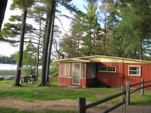 una cabaña roja en el bosque junto a un lago en Holiday Acres Resort, en Rhinelander