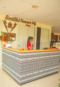 Een vrouw die aan een balie zit te praten met een mobiele telefoon bij Seatiki Resort Fiji On Coast in Sigatoka