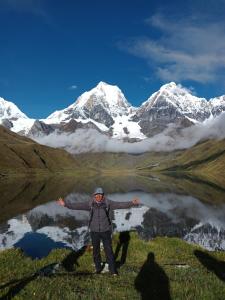a man standing in front of a mountain reflected in a lake at El Amauta de los Andes Lodging Erik House in Huaraz