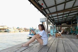 una ragazza seduta su un molo vicino all'acqua di Rub Lom Chom Klong Homestay a Chumphon