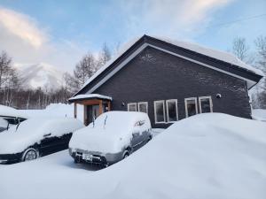 a house with snow covered cars parked in front of it at RuPow Lodge - walking distance to Rusutsu Resort in Rusutsu