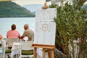 um sinal com duas pessoas sentadas numa mesa junto à água em Vila Perast Boutique Hotel em Perast