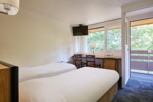 una camera d'albergo con due letti, una scrivania e una finestra di Kyriad Caen Nord - Hérouville-Saint-Clair a Hérouville-Saint-Clair