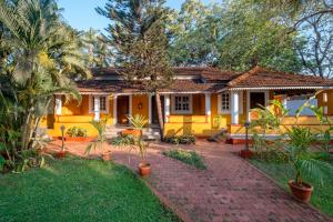 a yellow house with a brick walkway in front of it at Granpa's Inn Hotel Bougainvillea in Anjuna