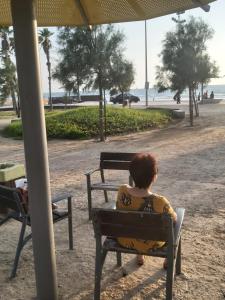 Eine Frau, die unter einem Schirm auf einer Bank sitzt. in der Unterkunft studio by the sea in Aschdod