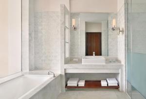 Le Meridien Jaipur Resort & Spa في جايبور: حمام مع حوض ومغسلة ومرآة