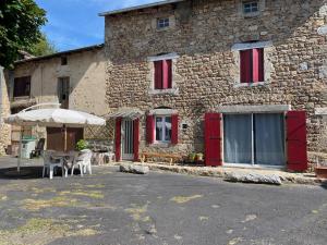 a stone building with red doors and a table and an umbrella at CHAMBRE D HOTES CHEZ DANY MAOWMAOW ET GARFIELD in Bellevue-la-Montagne