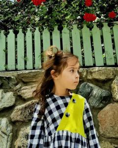 a little girl wearing a yellowpron standing in front of a fence at Guest house-Lile in Mestia