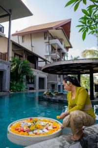 una mujer sentada junto a una piscina con una pizza en Sense Canggu Beach Hotel, en Canggu