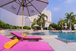 einen Pool mit lila Liegestühlen und einem Sonnenschirm in der Unterkunft TTC Hotel Phan Thiet in Phan Thiet