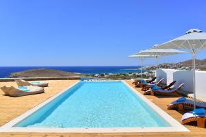 una piscina con sedie, ombrelloni e oceano di Horizon Villas ad Agios Ioannis