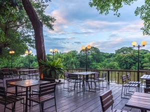 a deck with tables and chairs and trees at The Legacy River Kwai Resort in Kanchanaburi City