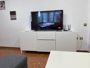 telewizor siedzący na białym centrum rozrywki w obiekcie Piso grande de 120 m2, a 15' de la playa en coche w mieście Huelva