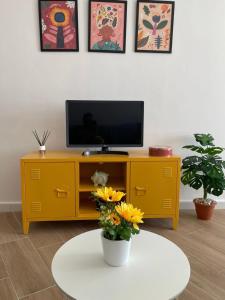 - un centre de divertissement jaune avec une télévision et des fleurs sur une table dans l'établissement Estudio con vistas, à Torremolinos