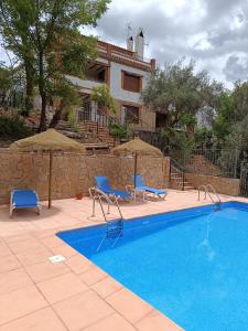 a swimming pool with two blue chairs and a house at CASA RURAL CURTIDORES in El Batán