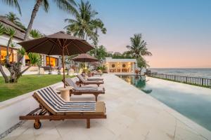 a row of lounge chairs and an umbrella next to a swimming pool at Villa Dahlia, 4 bed Oceanfront Retreat, Candidasa in Manggis