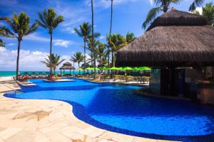 a swimming pool at a resort with palm trees and the ocean at Hotel Solar Porto de Galinhas in Porto De Galinhas